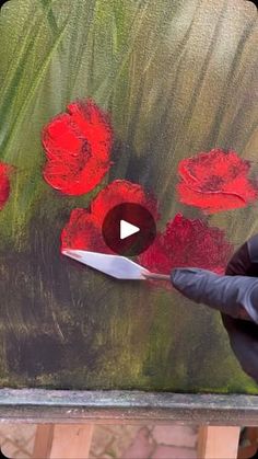 a woman is painting red flowers on a large piece of art with acrylic paint