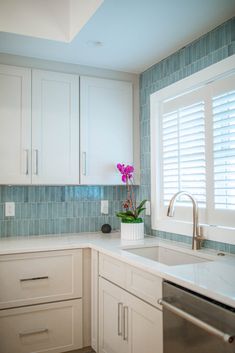 a kitchen with white cabinets and blue tile backsplashes, including a sink