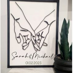 two hands holding each other in the shape of a heart on a white background next to a potted plant