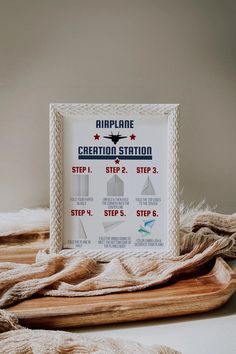 an airplane creation station sign sitting on top of a wooden tray next to a blanket