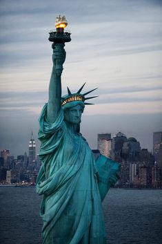 the statue of liberty is lit up at night in new york city, with manhattan behind it