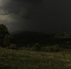 a dark sky is seen over the hills and trees in the distance, with storm clouds overhead