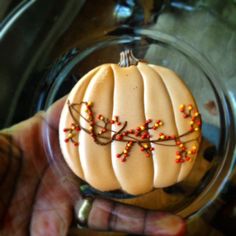 a hand holding a fake pumpkin on top of a glass plate