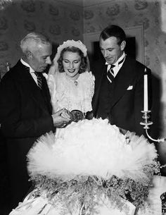 an old black and white photo of two men and a woman looking at a cake