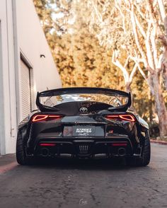 the rear end of a black sports car parked in front of a white garage door