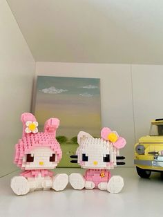 two hello kitty figurines sitting next to each other in front of a yellow truck