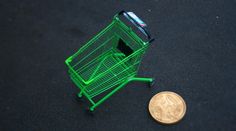 a small green shopping cart sitting next to a penny