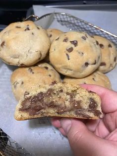 a hand holding a half eaten chocolate chip cookie in front of some cookies on a cooling rack