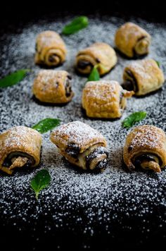 small pastries with powdered sugar and mint sprinkled around them on a black surface