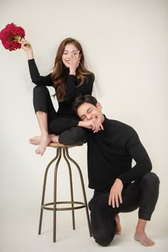 a man kneeling down next to a woman on top of a stool holding a flower