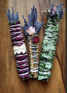 three bundles of dried flowers tied together on a wooden table with white and purple string