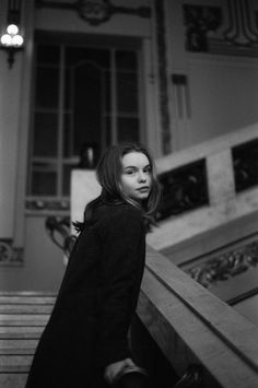 black and white photograph of a woman standing at the top of stairs in an old building