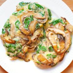 a white plate topped with mushrooms and spinach covered in sauce on top of a wooden table