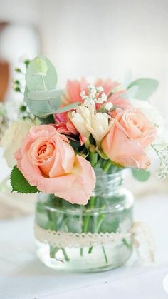 an arrangement of flowers in a mason jar on a white tableclothed table cloth