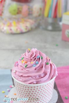 a cupcake with pink frosting and sprinkles sits on a table