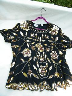 This is a beautiful 100% silk evening/formal wear short sleeve blouse by Stenay. Made in India, it is a size 24 W with a stunning beaded sequin trim, as shown in the photos. The beads are a green/brown, and the sequins are a gold and copperish. They seem to pick up surrounding colors in the light. Quite stunning and impressive. It is approx. 27" from armpit to armpit, 27" down the back, and 19" from shoulder to shoulder. Elegant Embellished Tops For Festive Season, Spring Formal Beaded Tops, Summer Formal Sequin Blouse, Formal Summer Sequin Blouse, Festive Embellished Tops For Night Out, Beaded Short Sleeve Top For Party, Elegant Beaded Tops For Party, Glamorous Beaded Party Blouse, Embellished Evening Blouse For Summer