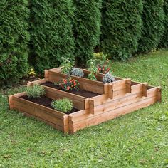 three wooden raised planters with plants in them on the grass next to some bushes