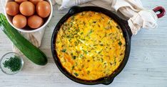 an omelet in a cast iron pan next to eggs and cucumbers