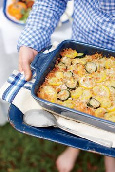 a person holding a blue casserole dish with zucchini and squash in it