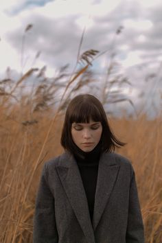 a woman standing in tall grass with her head turned to the side and eyes closed