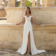 a woman in a white dress leaning against a stone wall