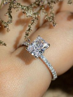 a woman's hand with a diamond ring on her finger and flowers in the background