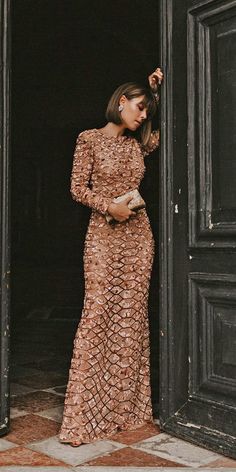 a woman standing in front of an open door wearing a long brown dress and heels