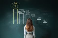 a woman standing in front of a chalkboard drawing on it with money and coins