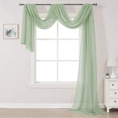 a white room with a window and green drapes on the windowsill in front of it