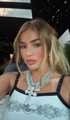 a woman with blonde hair wearing a white shirt and silver necklace, posing for the camera