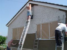 two men are painting the side of a house while another man stands on a ladder