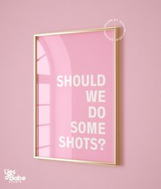 a pink poster with the words should we do some shots? in gold frame against a pink wall