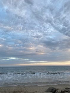 two people walking on the beach with surfboards in their hands, under a cloudy sky