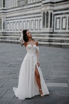 a woman in a white wedding dress standing on the street with her arms behind her head