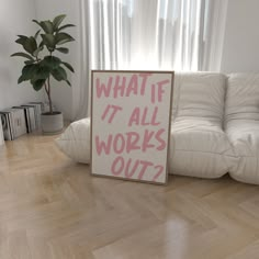 a sign sitting on the floor in front of a white couch with a potted plant next to it