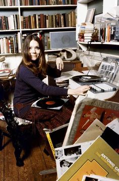 a woman sitting on the floor in front of a record player and bookshelf