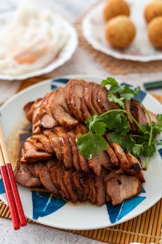 sliced meat on a plate with chopsticks next to it and other food items