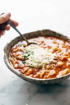 a person is holding a spoon over a bowl of pasta and sauce with parmesan cheese on top