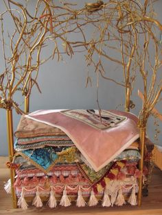 a bed covered in lots of blankets and tassels next to a tree branch