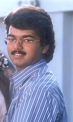 a man with glasses and a moustache standing next to a woman in a blue striped shirt