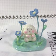 a figurine of a bunny sitting in the grass with blue flowers on it