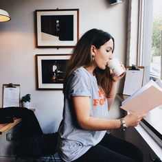 a woman sitting at a piano drinking from a cup and reading a book in front of a window