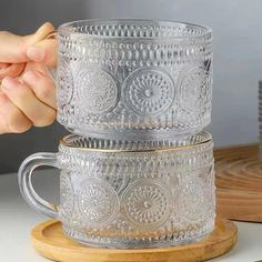 two clear glass mugs sitting on top of a wooden stand next to each other