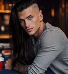 a man with long hair and piercings sitting at a table next to a cup