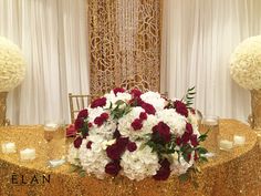 a gold table with white and red flowers, candles and vases on the side