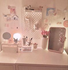 a white desk topped with lots of clutter next to a wall mounted mirror and lamp