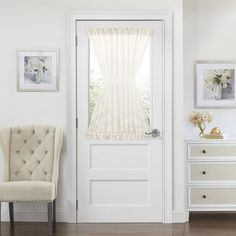 a white chair sitting in front of a door next to a window with sheer curtains