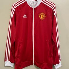 a red and white jacket hanging up on a wall next to a hanger with the manchester united logo