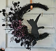 a wreath with a cat and flowers hanging on the front door to decorate it for halloween