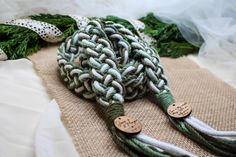 a green and white knoted rope with two wooden tags on it sitting on a burlap surface